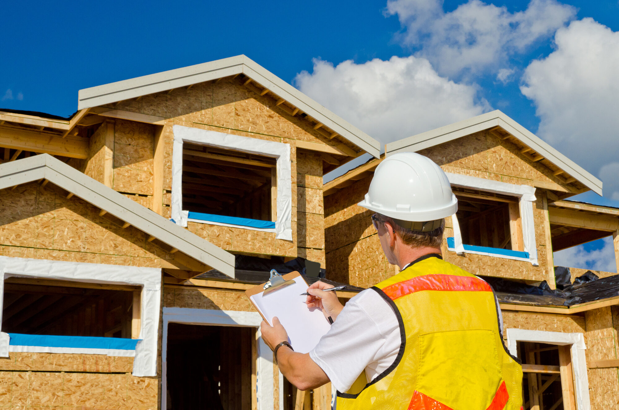 A man in a hard hat standing in front of an house holding a clipboard in his hand